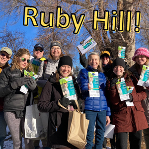 Group of smiling people outdoors with blue sky, they're holding up flyers saying "Denver Digs Trees"